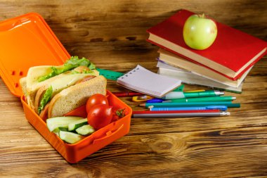 Okul konseptine geri dönelim. Okul malzemeleri, kitaplar, elma ve beslenme çantası içinde sandviçler ve ahşap bir masada taze sebzeler.