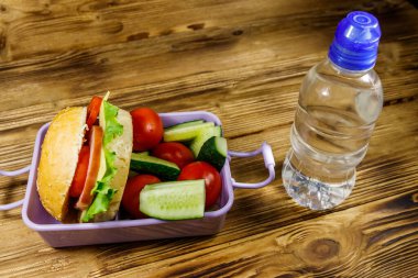 Bir şişe su, hamburgerler ve taze sebzeler ahşap bir masada.