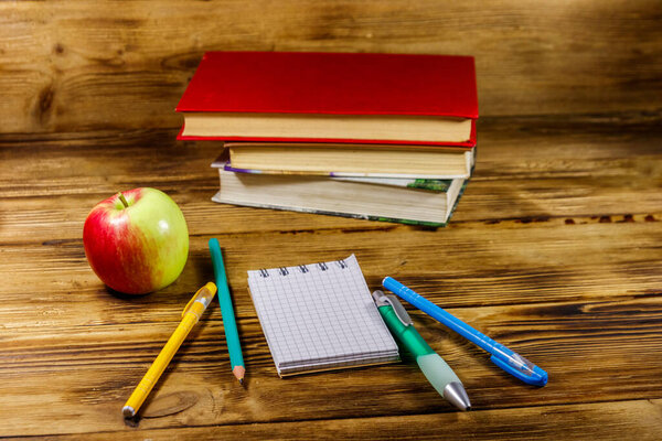 Stack of books, notepad, pens, pencils and apple on wooden desk. Back to school concept