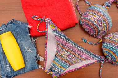 Ahşap arka plan üzerinde beachwear kümesi. Güneş kremi, havlu, mayo ve jean şort. Yaz tatil kavramı