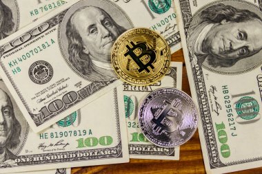 Altın ve gümüş paralar ve 100 dolarlık banknotlar ahşap masada.