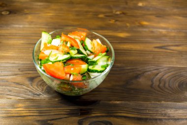 Domatesli taze salata, salatalık, soğan, maydanoz ve ahşap masadaki cam kasede dereotu.