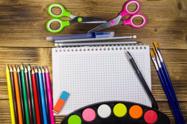 Okul Kırtasiye malzemeleri kümesi. Boş defter, kalem, kalem, suluboya boyalar, makas, Boya fırçaları, silgi ahşap masa üzerinde renkli. Geri okul kavramı