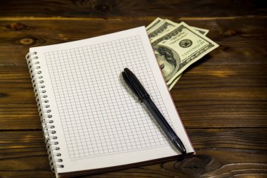 Tahta masanın üzerinde tükenmez kalem ve dolar banknotları olan defter. Para biriktirme kavramı