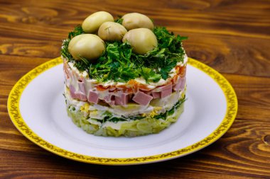 Geleneksel Rus katmanlı salata haşlanmış patates, havuç, yumurta, sosis, yumuşak peynir, marine edilmiş mantar ve ahşap masada mayonez.