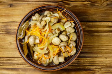Tahta masadaki seramik kasede havuç, soğan ve baharatla marine edilmiş lezzetli mantarlar. Üst görünüm