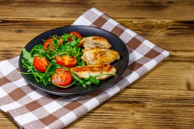 Kızarmış tavuk göğsü, taze roka salatası ve ahşap masada vişneli domates.