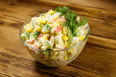 Yengeç çubuklu salata, mısır, salatalık, yumurta, pirinç ve mayonez ahşap masada.