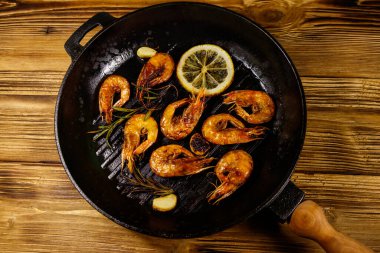 Baharatlı ızgara karides, biberiye ve limon ahşap bir masada ızgara kızartma tavasında. Üst görünüm