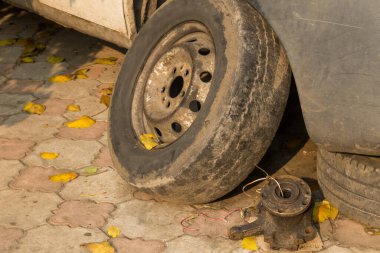 Tamir için beyaz bir arabanın yanındaki eski tekerlek.