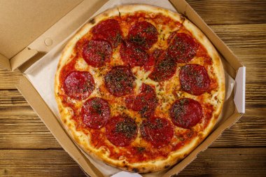 Tahta bir masanın üzerindeki karton kutuda nefis taze pizza. Üst Manzara. Yemek teslimatı, fast food, pizza teslimatı.