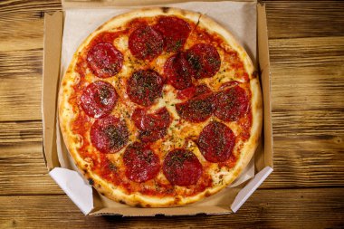 Tahta bir masanın üzerindeki karton kutuda nefis taze pizza. Üst Manzara. Yemek teslimatı, fast food, pizza teslimatı.