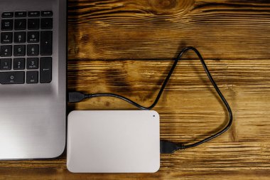 Harici HDD, tahta bir masadaki dizüstü bilgisayara bağlı. Üst Manzara. Veri depolama kavramı