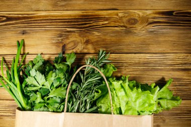 Yeşil soğanlı kağıt torbası, biberiye, marul yaprakları ve ahşap masada maydanoz. Üst Manzara. Sağlıklı gıda ve market alışverişi kavramı