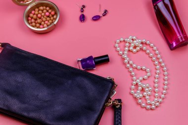 Debriyaj çantası, inci kolye, küpeler, oje, ruj topları ve pembe arka planda bir şişe parfüm. Güzellik ve moda konsepti. Düz yatıyordu