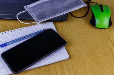 Bilgisayarda fare, akıllı telefon, defter, kalem ve tıbbi maske var. Karantina sırasında evde eğitim ve çalışma kavramı. Evde kal. Coronavirus covid-2019 'dan koruma