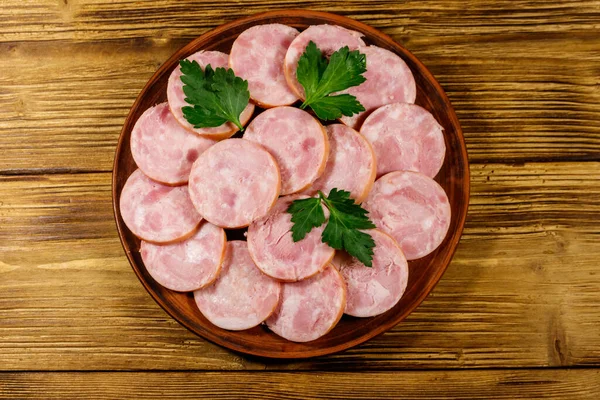 Ham sausage on a plate on wooden table. Top view