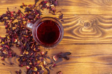 Ahşap masada bir bardak kırmızı amber çayı (carcade, roselle).