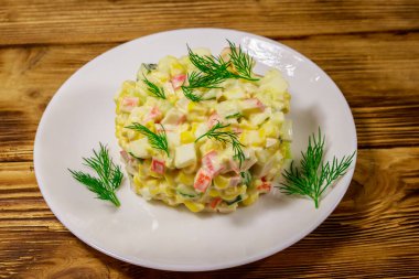 Yengeç çubuklu salata, tatlı mısır, salatalık, yumurta ve mayonez ahşap masada.