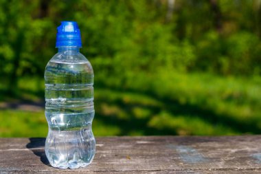 Doğanın arka planında, ahşap bir masanın üzerinde taze içme suyu olan plastik şişe.