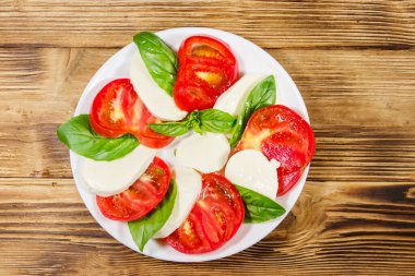 Domatesli İtalyan caprese salatası, ahşap bir masada mozzarella peyniri ve fesleğen. Üst görünüm