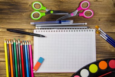 Okul Kırtasiye malzemeleri kümesi. Boş defter, kalem, kalem, suluboya boyalar, makas, Boya fırçaları, silgi ahşap masa üzerinde renkli. Geri okul kavramı