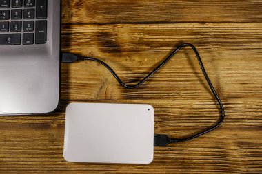Harici HDD, tahta bir masadaki dizüstü bilgisayara bağlı. Üst Manzara. Veri depolama kavramı