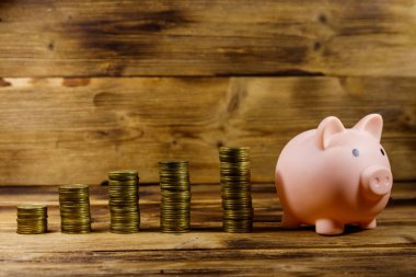 Pembe domuz kumbarası ve tahta arka planda yığınla bozuk para. Para biriktirme kavramı