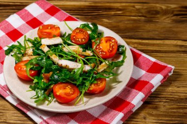 Lezzetli tavuk göğsü salatası, taze roka ve ahşap masada kiraz domatesleri.
