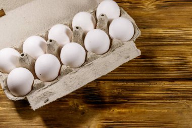 Tahta masadaki karton yumurta kutusunda çiğ tavuk yumurtası. Üst görünüm