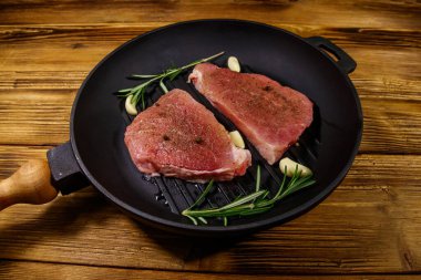 Biberiye, sarımsak ve baharatlı çiğ domuz bifteği ahşap masada ızgara demir tavada pişirilmeye hazır.