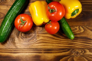 Mutfak masasında bir yığın taze sebze. Ahşap zemin üzerinde olgun domates, biber ve salatalık. Üst görünüm