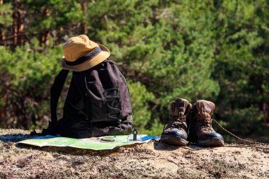Yürüyüş botları, şapkası, pusulası ve haritası olan turist sırt çantası çam ormanında. Yürüyüş teçhizatı. Seyahat kavramı