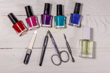 Beyaz ahşap arka planda temel manikür aletleri seti. Tırnak makası, tırnak makası, tırnak törpüsü ve oje şişeleri.