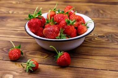 Tahta bir masada beyaz kasede taze olgun çilek.