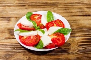 Domatesli İtalyan caprese salatası, ahşap bir masada mozzarella peyniri ve fesleğen.