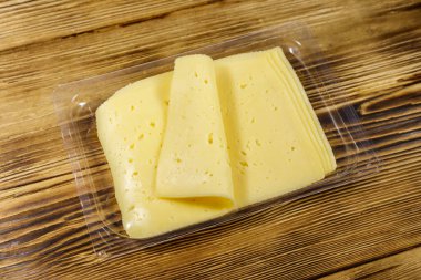 Tek kullanımlık plastik bir kutuda dilimler halinde peynir, ahşap bir masada.