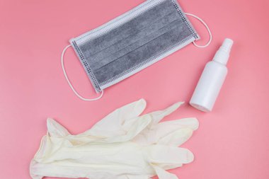 Koruyucu tek kullanımlık tıbbi maske, eldivenler ve pembe arka planda el dezenfektanı. Üst görünüm