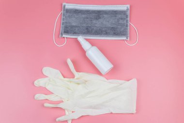 Koruyucu tek kullanımlık tıbbi maske, eldivenler ve pembe arka planda el dezenfektanı. Üst görünüm