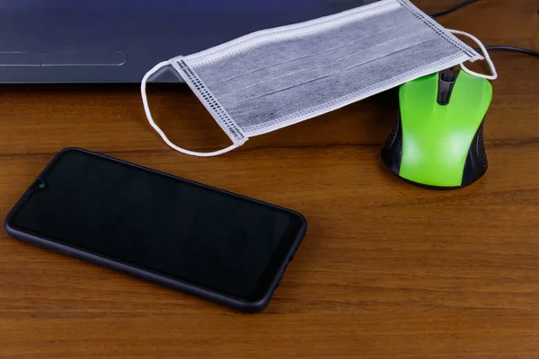 Laptop with mouse, smartphone and medical mask on a desk. Concept of home schooling and working from home during quarantine. Stay at home. Protection from coronavirus covid-2019