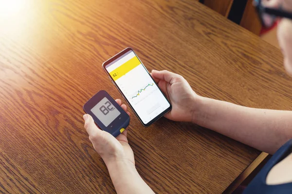 Geleneksel glukometredeki glikoz seviyesini ve modern teknoloji uzaktan sensöründeki cep telefonunu karşılaştıran kadın.