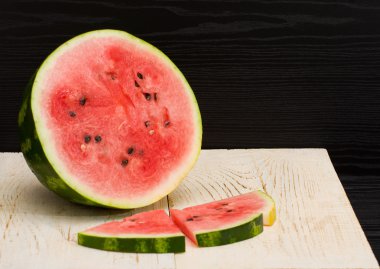 İkiye ayırmak karpuz ve dilimleri bir ahşap masa, siyah arka plan üzerinde