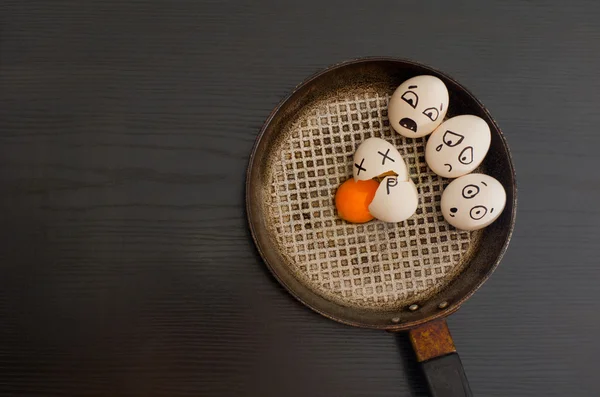 Huevos con las emociones dibujadas, huevo roto en el centro de la sartén, mesa negra — Foto de Stock