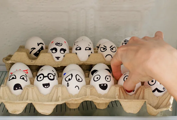 Huevos con emociones pintadas en el refrigerador, una mano femenina toma uno de ellos — Foto de Stock