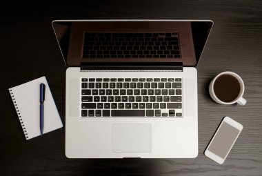 Üstten görünüm açık laptop, defter kalem, akıllı telefon ve kahve siyah ahşap bir masa üzerinde bir kupa ile