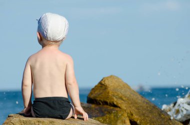 Küçük çocuk yüzme gövdeleri, mavi gökyüzü, metin için yer deniz kıyısına sırtında bir rock ile oturan