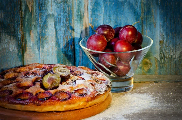 Taart met pruimen en verse pruimen in een kom op de vintage blauwe achtergrond — Stockfoto