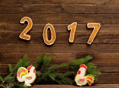 Yeni yıl kavramı. Şekil 2017 ve gingerbread, köknar dalı ahşap arka plan üzerinde gelen iki horoz.