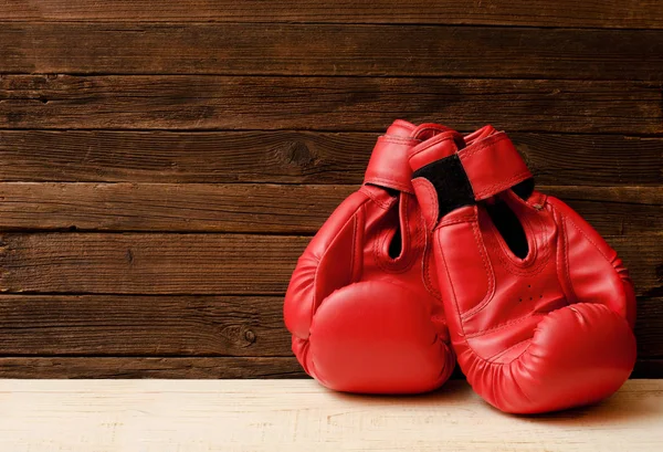 Dos guantes de boxeo rojos en un lado del marco sobre un fondo marrón de madera, espacio vacío —  Fotos de Stock