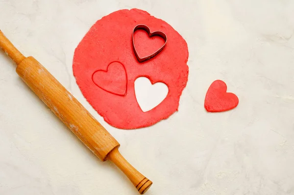 Bir oklava ve beyaz bir tablo kalpleri dışarı kesim ile kırmızı hamur — Stok fotoğraf